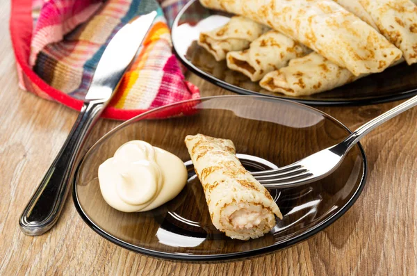 Pancake rolls in brown plate, knife, piece of pancake on fork, m