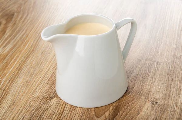 White pitcher with fermented baked milk on brown wooden table