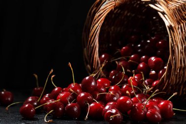 Siyah bir arka plan üzerinde dağınık olgun kiraz ve hasır sepet