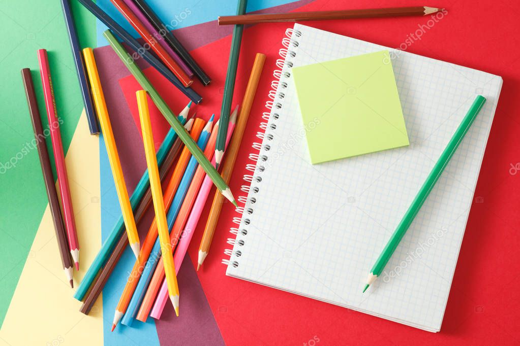 Notebook and pencils lie on colored paper. 