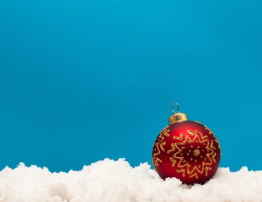Mavi arka planda kar üzerinde noel topu