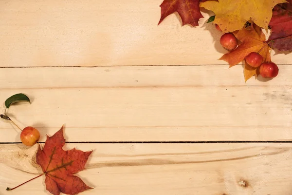 Hojas de arce y manzanas rojas en una mesa de madera — Foto de Stock