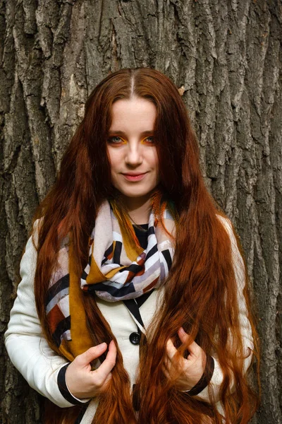 Mujer con el pelo largo y rojo y maquillaje brillante cerca de un árbol —  Fotos de Stock