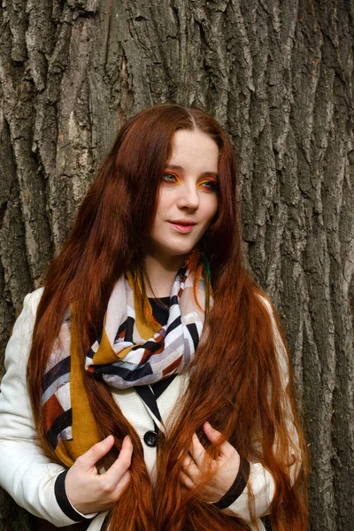 Woman with long red hair and bright makeup near a tree — Stock Photo, Image