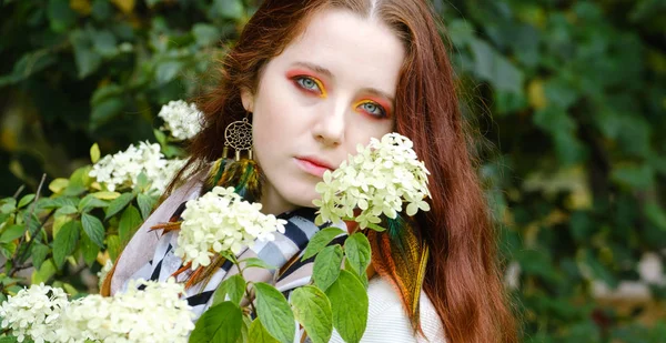Woman with red hair and bright makeup near flowers on the nature — Stock Photo, Image