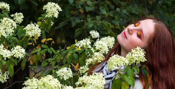 Woman with red hair and bright makeup near flowers on the nature — Stock Photo, Image