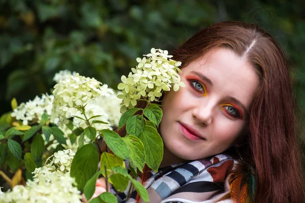 Woman with red hair and bright makeup near flowers on the nature — Stock Photo, Image