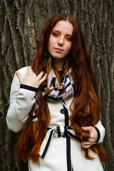 Mulher com cabelo vermelho longo e maquiagem brilhante perto de uma árvore — Fotografia de Stock