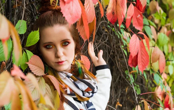 Mulher com cabelo vermelho e maquiagem brilhante perto das folhas de outono de — Fotografia de Stock