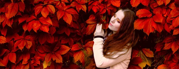 Woman with long red hair and bright makeup near the red leaves o — Stock Photo, Image