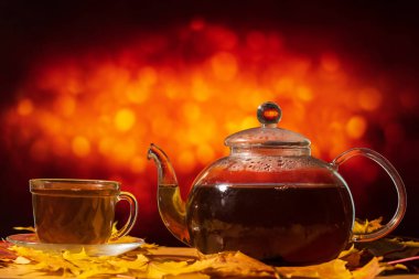 Çaydanlık ve kupa, portakal rengi bir sırtta sonbahar yaprakları olan bir masada.