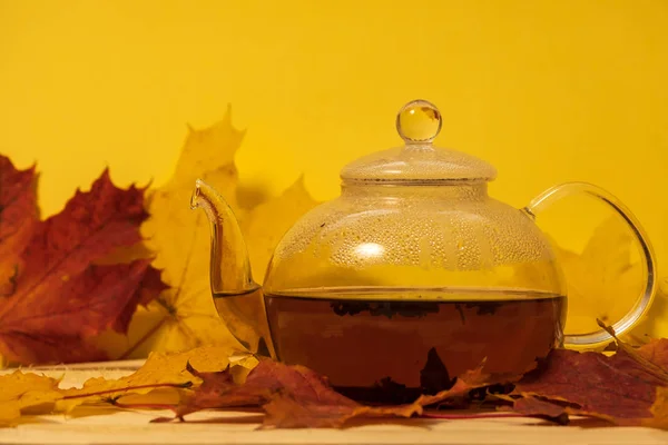 Konvice na stole s podzimními listy na žlutém pozadí — Stock fotografie