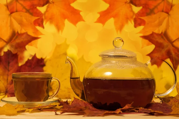 Teapot and cup on a table with autumn leaves on a yellow backgro — Stock Photo, Image