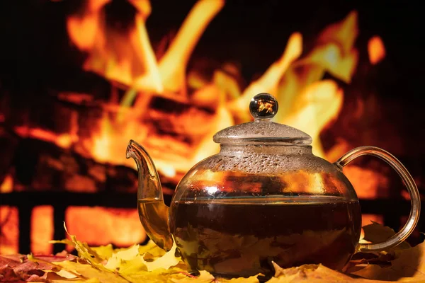 Teapot on a table with autumn leaves on a background of a burnin — Stock Photo, Image