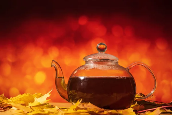 Teapot on a table with autumn leaves on a orange background — Stock Photo, Image
