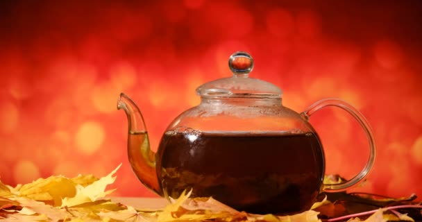 Teapot on a table with autumn leaves on a orange background — ストック動画
