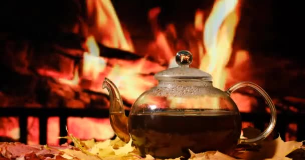 Teapot on a table with autumn leaves on a background of a burning