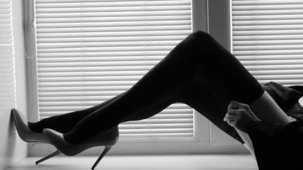 Lunghe gambe femminili in calze nere e scarpe col tacco alto su un davanzale vicino alla finestra con persiane — Video Stock