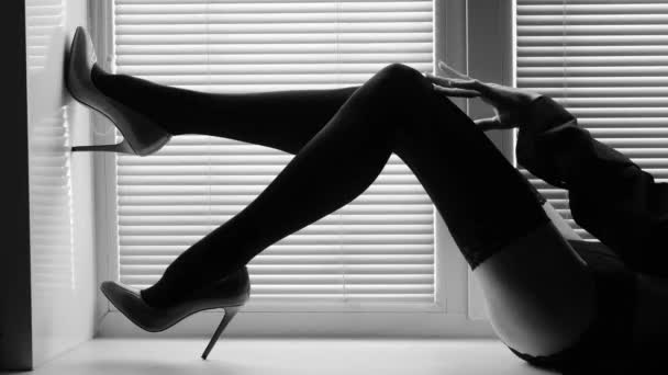 Lange vrouwelijke benen in zwarte kousen en hoge hakken op een vensterbank bij het raam met rolluiken — Stockvideo