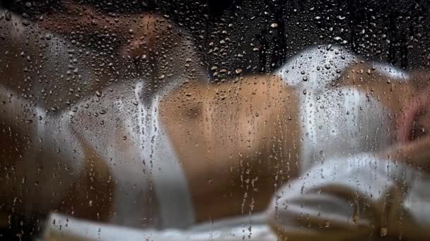 Blurry female body in white underwear behind wet glass with raindrops — Stock Video