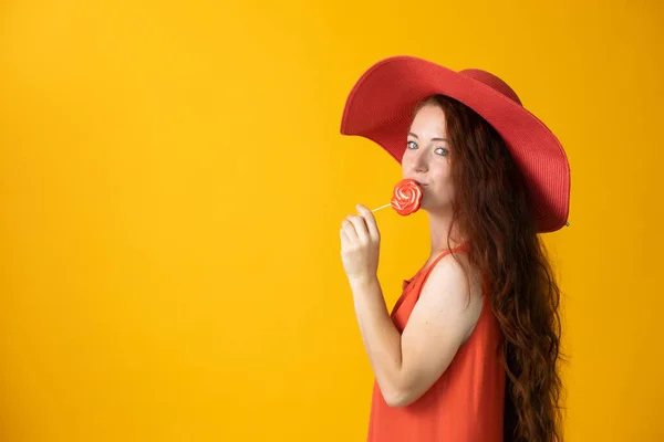 Piękna Kobieta Długimi Włosami Dużym Czerwonym Kapeluszu Lizakiem Żółtym Tle — Zdjęcie stockowe