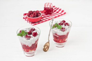 Chia tohum Hindistan cevizi sütü puding ile yulaf ezmesi granola, ahududu reçeli, Hindistan cevizi cips ve cam beyaz ahşap zemin üzerine nane