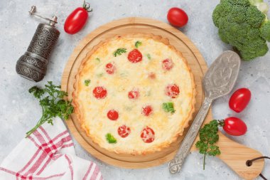 Brokolili kiş turtası, kiraz domatesleri, somon balığı, peynir, ahşap kesim tahtasında kremalı yumurta ve gri beton arka plan.