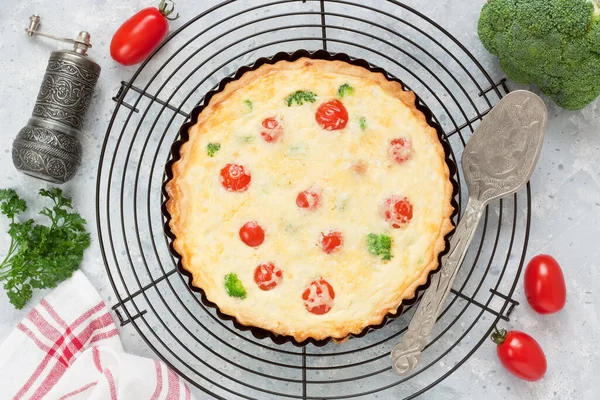 Brokolili kiş turtası, domates, somon balığı, peynir, kremalı yumurta metal soğutma rafında ve gri beton arka planda.