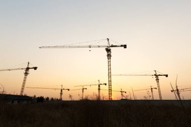 Günbatımı arka planında inşaat vinçleri
