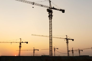 Günbatımı arka planında inşaat vinçleri