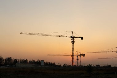 Günbatımı arka planında inşaat vinçleri