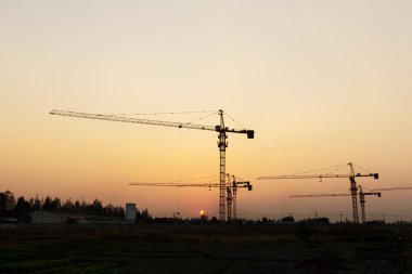 Günbatımı arka planında inşaat vinçleri