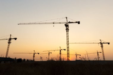 Günbatımı arka planında inşaat vinçleri