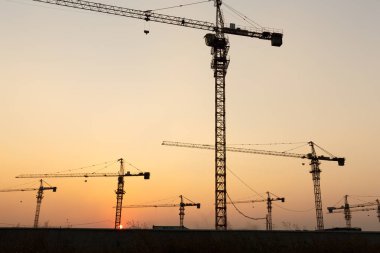Günbatımı arka planında inşaat vinçleri
