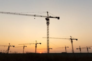 Günbatımı arka planında inşaat vinçleri