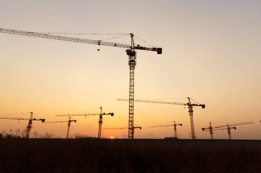 Günbatımı arka planında inşaat vinçleri