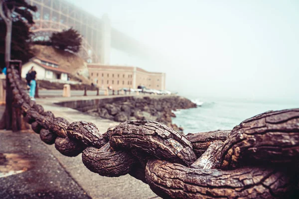 Golden Gate Bridge in the fog as seen from behind a railing chain at the Presidio. — Stockfoto