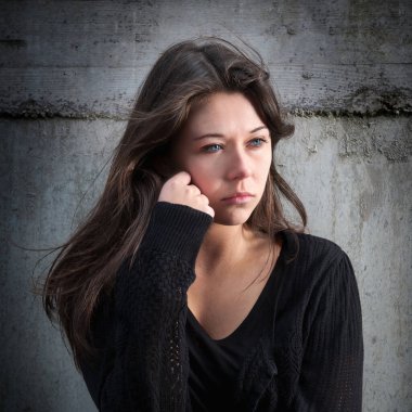Outdoor portrait of a sad teenage girl looking thoughtful about troubles in front of a gray wall clipart