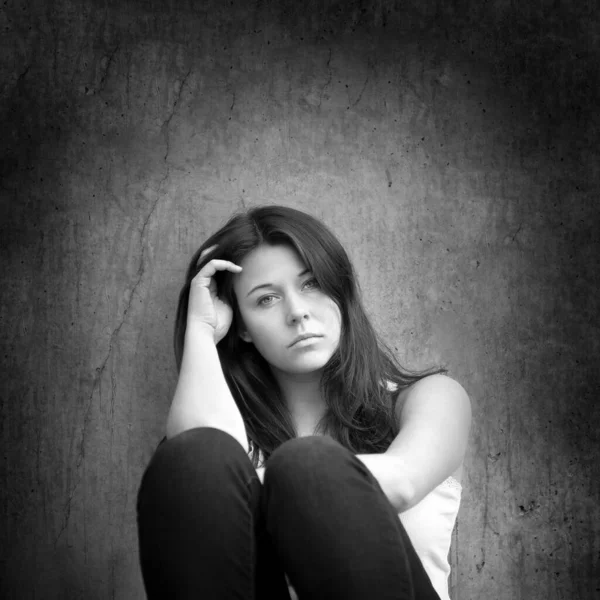 暗い灰色の壁の前でのトラブルについて思慮深く見て悲しい十代の女の子のモノクロームの肖像画 — ストック写真