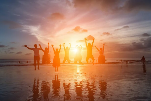 Groep van gelukkige vrienden springen op het strand tegen zonsondergang — Stockfoto