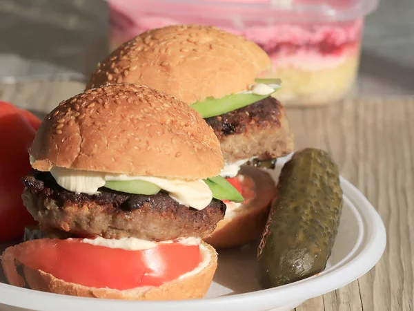 meat patty with fresh tomatoes and cucumbers in a bread bun lying on a rustic table, sandwich