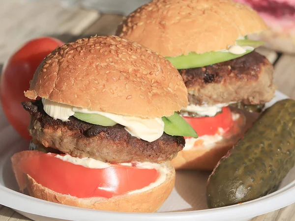 meat patty with fresh tomatoes and cucumbers in a bread bun lying on a rustic table, sandwich