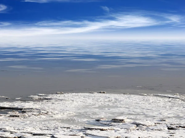 雪に覆われた海岸と冬の空の下で貯留層の氷のような水 — ストック写真