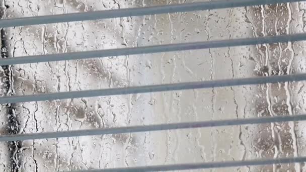 stock video raindrops flow down the window glass with plastic blinds