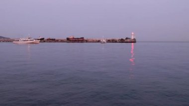 Bir ticaret gemisinin hareketi ve limanın su alanındaki iskelede titreşen bir deniz feneri.