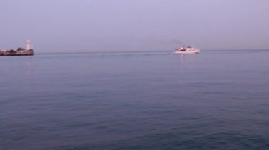 Bir ticaret gemisinin hareketi ve limanın su alanındaki iskelede titreşen bir deniz feneri.