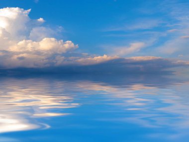 Sakin bir denizin yüzeyinde güneşli bulutlu bir gökyüzünün yansıması.