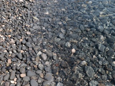 Bir çakıl taşı plajının yüzeyi ve berrak deniz suyu dalgaları.