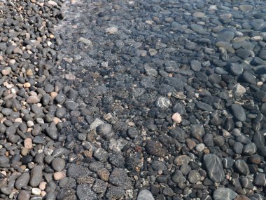 Bir çakıl taşı plajının yüzeyi ve berrak deniz suyu dalgaları.