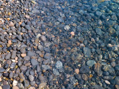 Bir çakıl taşı plajının yüzeyi ve berrak deniz suyu dalgaları.